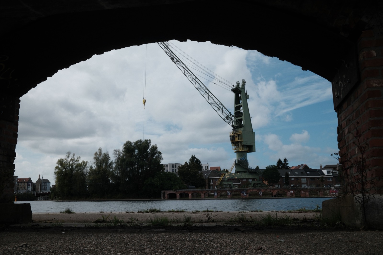 Oude havenkraan aan het water, gezien door de boog van een brug